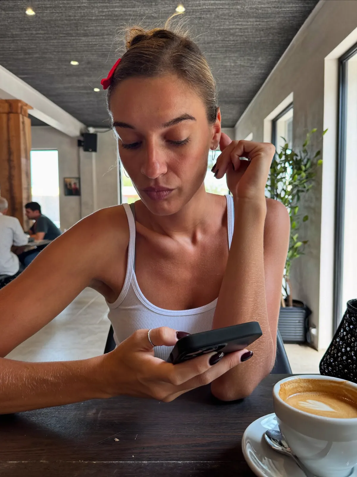 A woman slouched forward glancing at her phone at a cafe